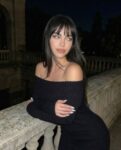 Woman in a black off-the-shoulder dress leaning on a stone railing at night