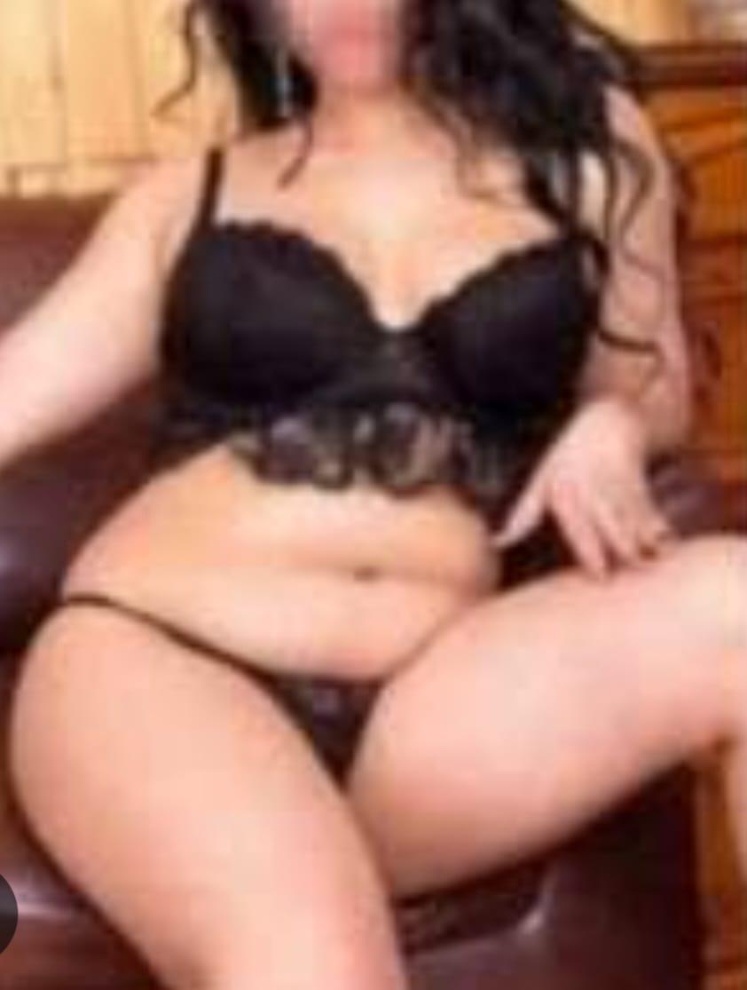 Woman in black lace lingerie sitting on a chair, with her legs crossed and arms resting on her lap.